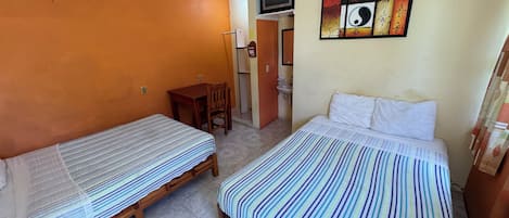 A room with two single beds, a desk, a chair, a television, and a bathroom.