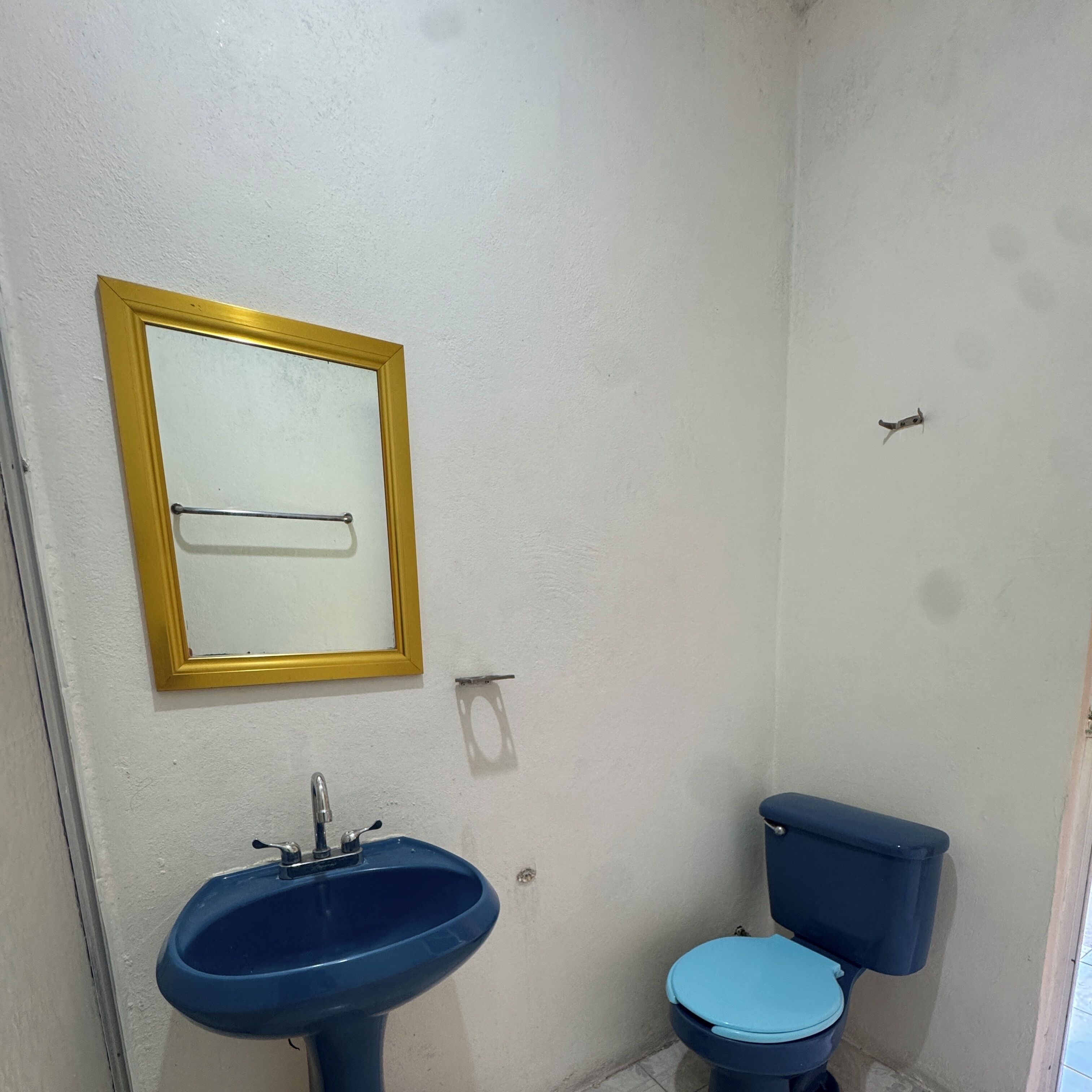 Ein Badezimmer mit einem blauen Waschbecken, einer Toilette und einem Spiegel mit goldener Rahmung.