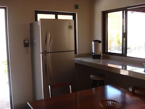 A compact kitchen with a refrigerator, a coffee maker, and a window providing a view of the outdoors. - Hostel Viatger Inn (Campeche)