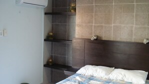 Quarto com cama, prateleira com objetos decorativos, lixeira e ar condicionado.