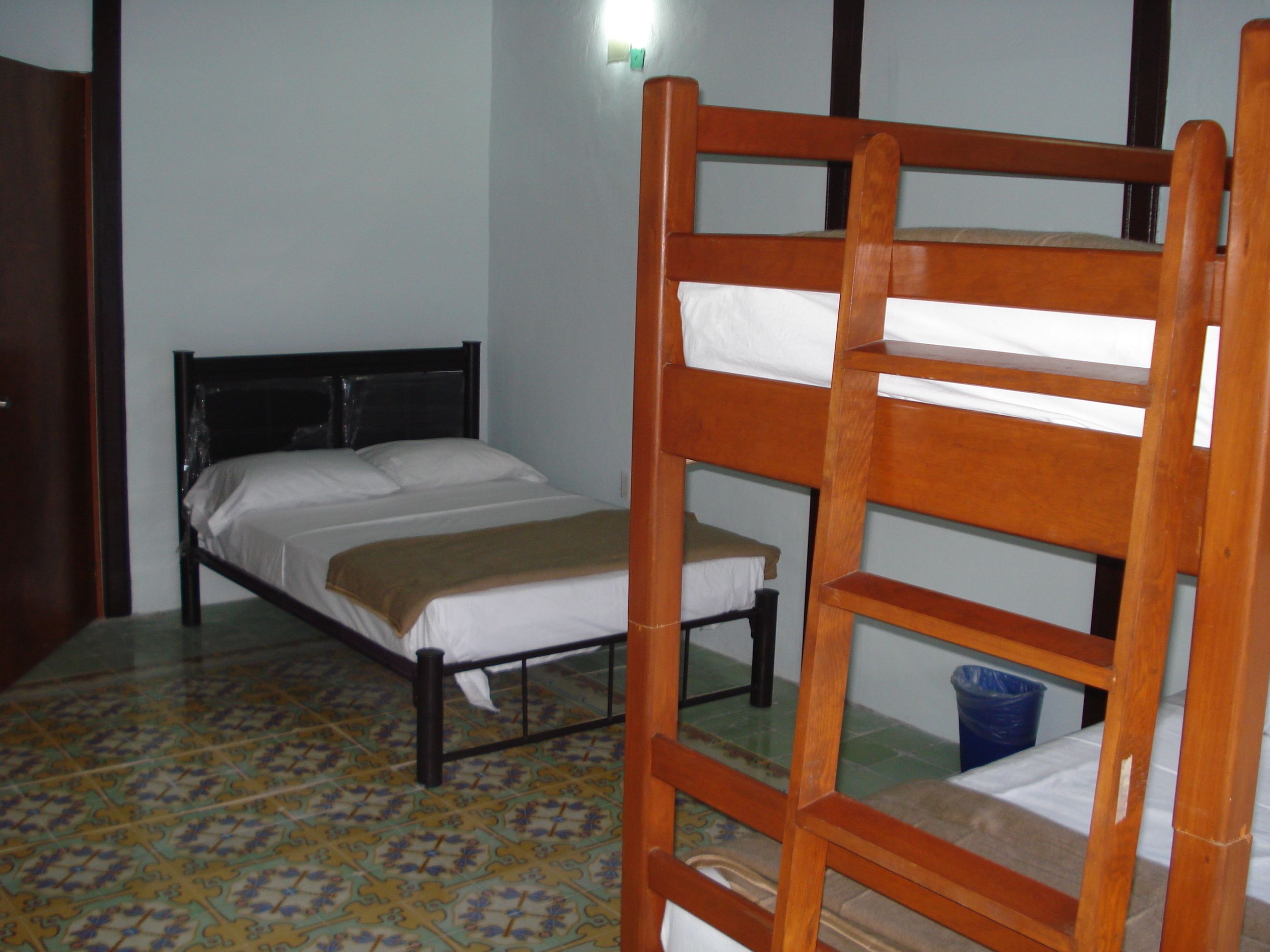 Una cama individual con cabecera de madera y colchón sobre suelo de baldosas.