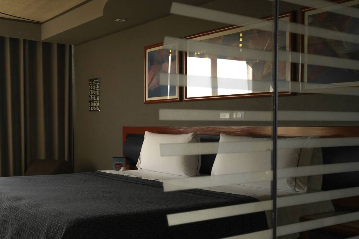 A hotel room with a bed, a nightstand, a window with curtains, and a wall with framed artwork.