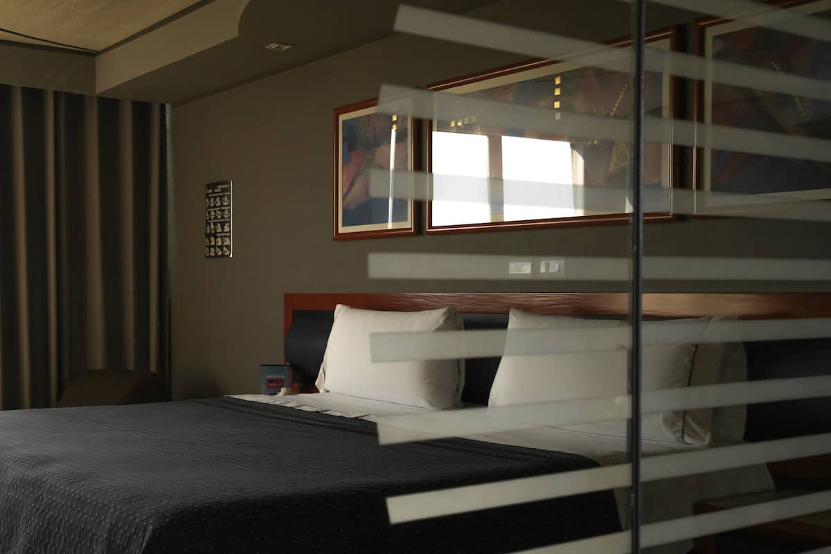 A hotel room with a large bed, a window with curtains, a bedside table, and a wall-mounted artwork.