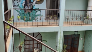 Un edifici de diverses plantes amb un mural al pis superior, una escala amb barana de ferro i plantes en testos als balcons.