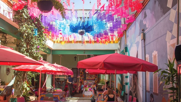 Una zona d'esmorzar a l'aire lliure amb taules i cadires, ombrel·les vermelles i decoracions penjants.