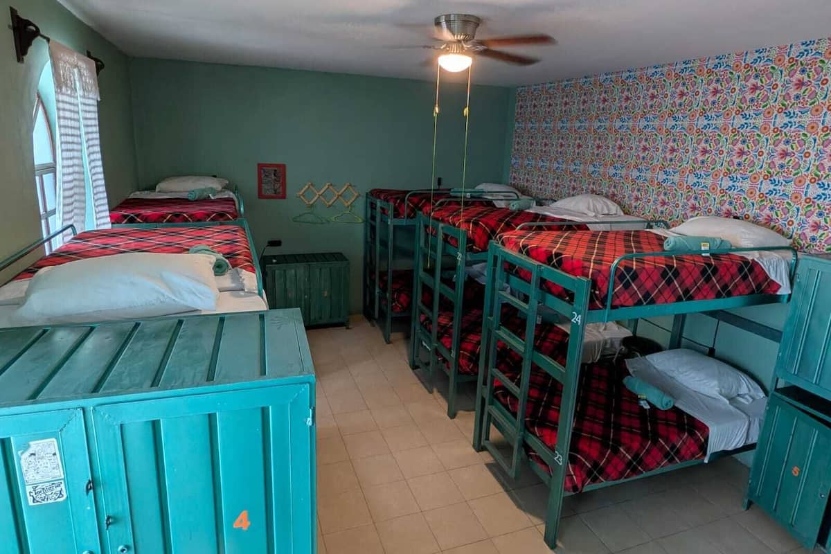 Um quarto de dormitório com beliches, ventilador de teto e janela com cortinas.