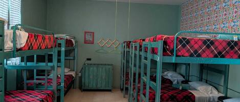 A dormitory room with bunk beds, a ceiling fan, a small cabinet, and a colorful wall pattern.
