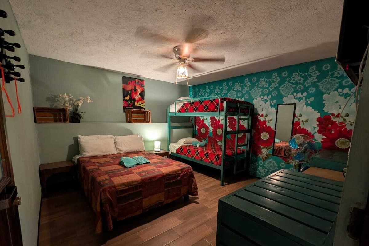 Um quarto com beliche, escrivaninha, ventilador de teto e papel de parede floral.