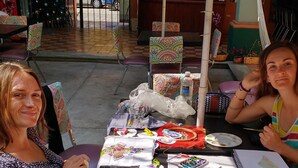 Dues persones assegudes a una taula amb diversos materials d'art, com pintura, pinzells i un telèfon mòbil.