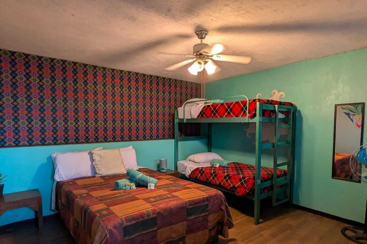 Quarto com beliche, parede estampada, ventilador de teto e piso de madeira.