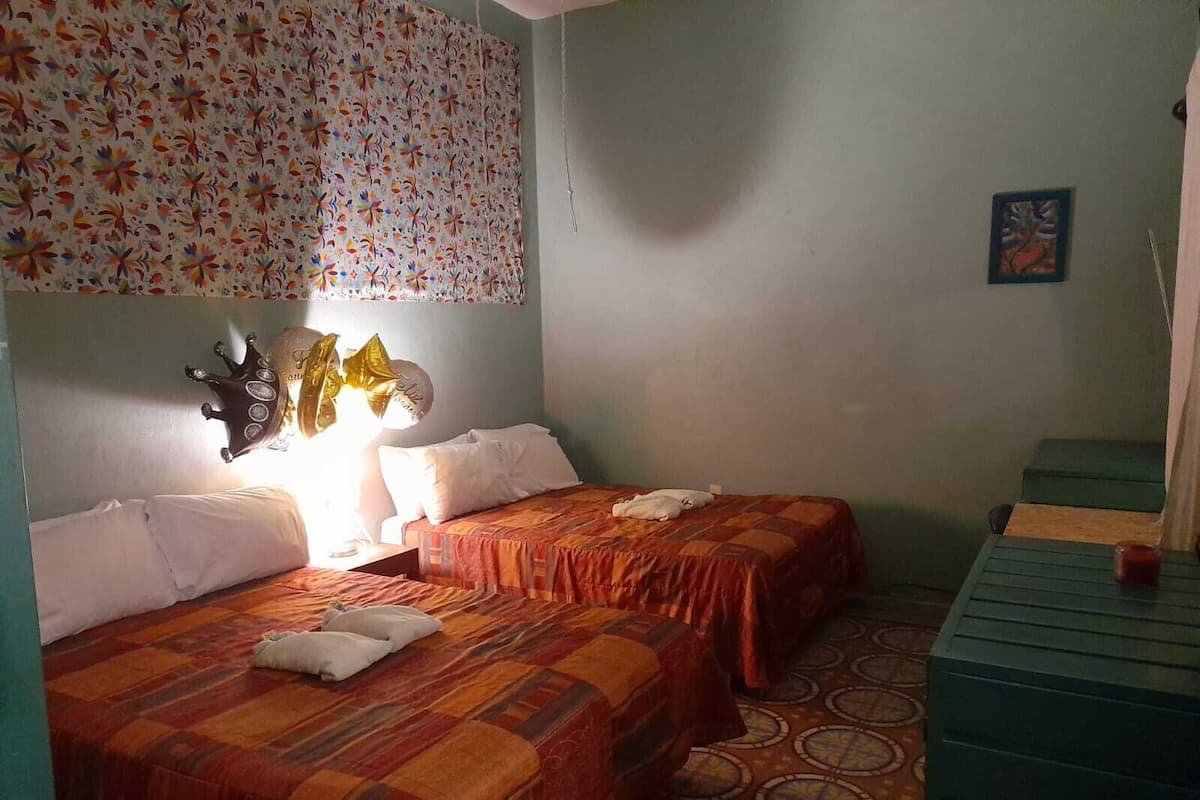Quarto com duas camas, parede estampada, uma mesinha e uma cadeira.