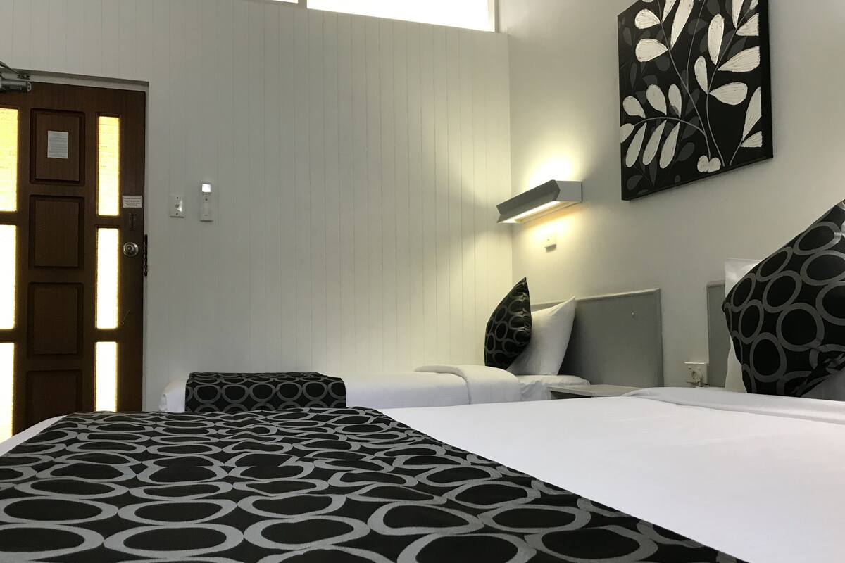 Quarto de hotel com cama, mesa de cabeceira, luminária na parede e porta com iluminação.