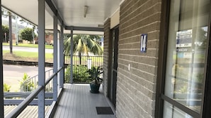 A covered outdoor area with a wooden deck, a potted plant, and a view of the street.