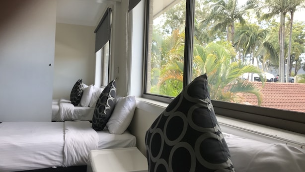 A hotel room with a large window, a sofa with patterned cushions, and a view of palm trees and parked cars outside.