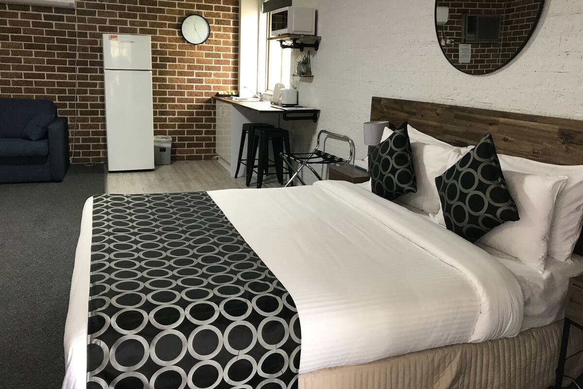 Quarto de hotel com cama, escrivaninha, cadeira, sofá e parede de tijolos.