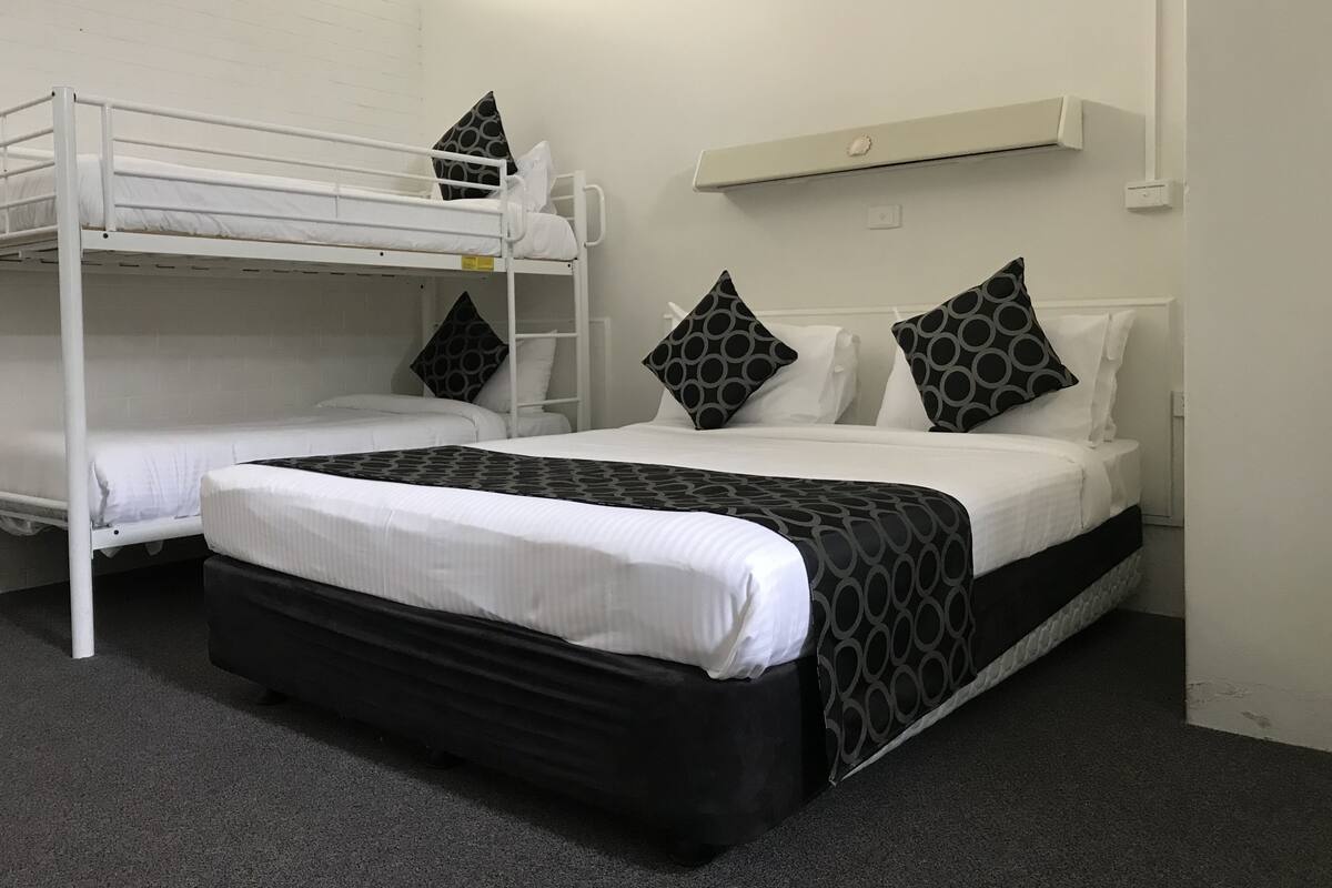 Quarto com beliches, uma cama individual e um pequeno aparelho de ar condicionado na parede.