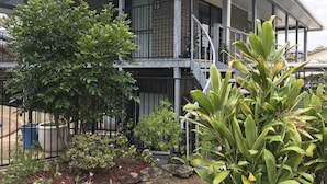 A two-story building with a balcony, surrounded by various plants and a garden area.
