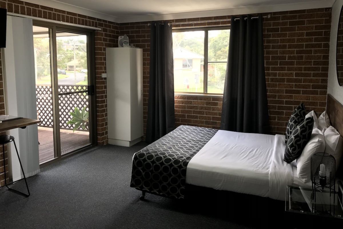 Quarto de hotel com cama, escrivaninha, guarda-roupa e varanda com vista para o exterior.