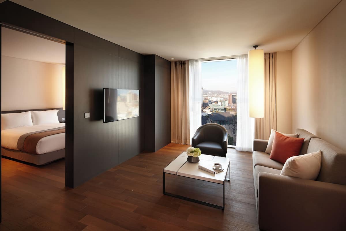 Une chambre d’hôtel moderne équipée d’un lit, d’un canapé, d’une table basse, d’une télévision et d’une grande fenêtre donnant sur la ville.