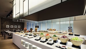 Buffet amb diversos plats i cuelles, zona de seients amb taules i cadires, i una cuina moderna al fons.