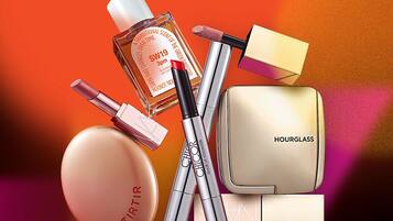 A collection of cosmetic products including a perfume bottle, makeup brushes, lipstick, and a compact powder case.
