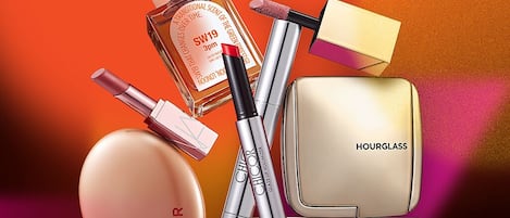Eine Auswahl an Kosmetikprodukten, darunter ein Parfümflakon, Make-up-Pinsel, Lippenstift und ein Puderdose-Etui.