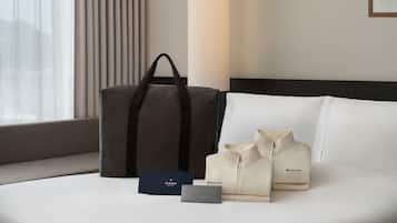 Una cama con una bolsa gris, dos bolsas color beige y una caja azul con texto en una habitación de hotel.