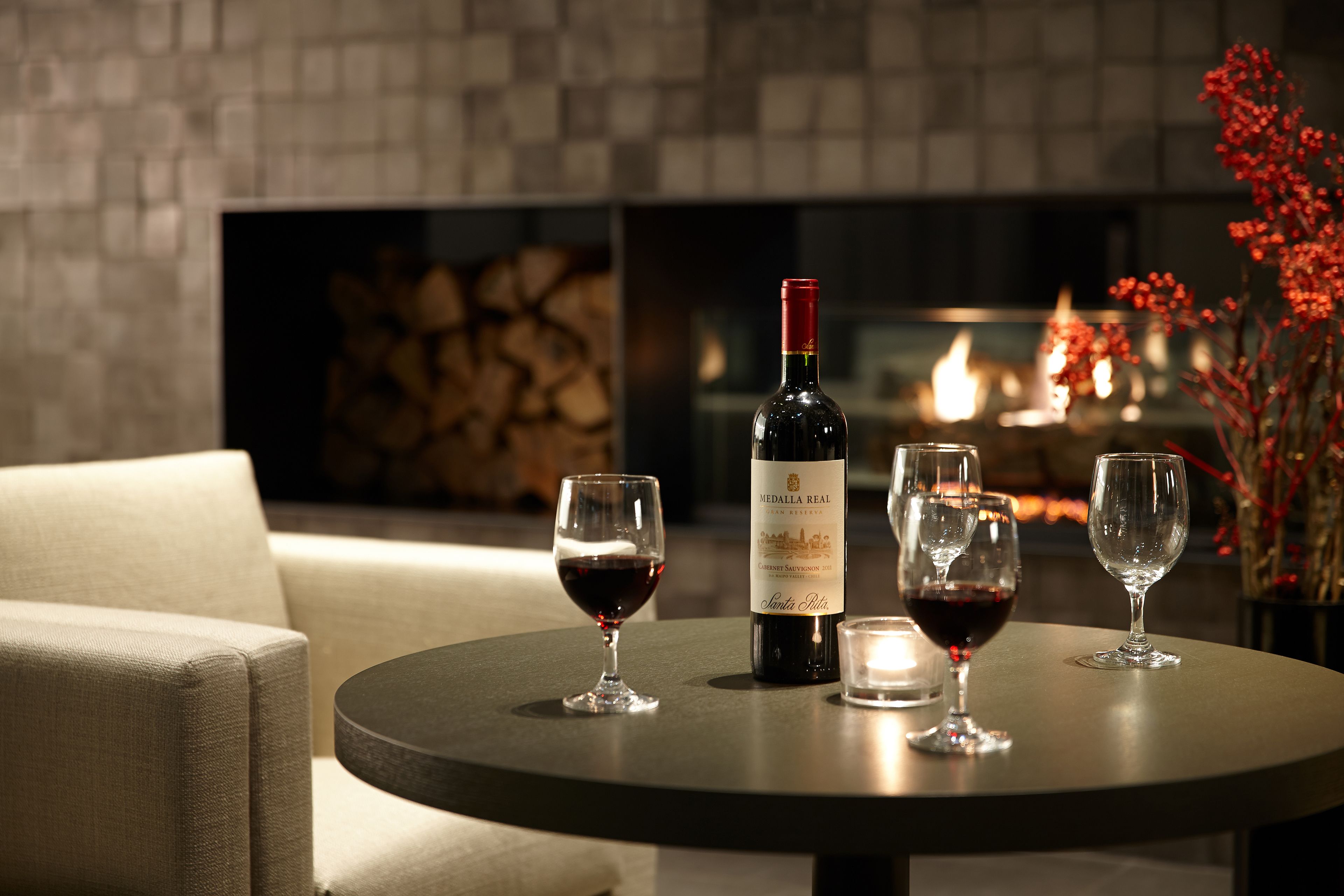 A round table with a bottle of wine, two glasses of red wine, and a candle.