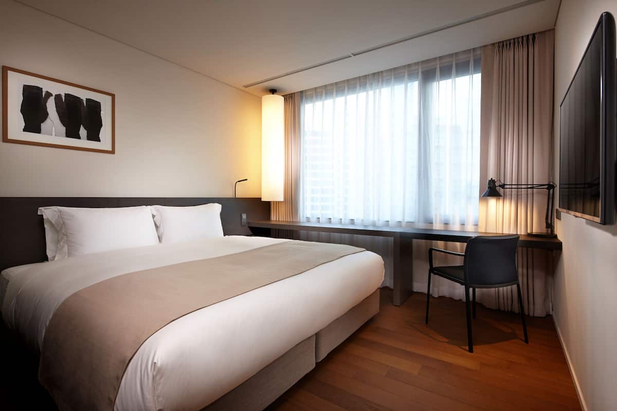 Une chambre d’hôtel avec un grand lit, un bureau avec une chaise, un téléviseur à écran plat et une fenêtre avec des rideaux.