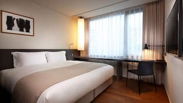 A hotel room with a large bed, a desk with a chair, a flat-screen TV, and a window with curtains.