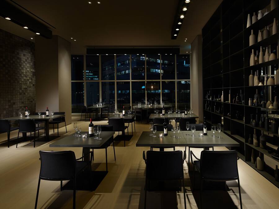 Un restaurante moderno con mesas dispuestas para comer, un ventanal con vistas a la ciudad y una pared decorada con jarrones.