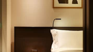 A hotel room with a bed, a nightstand with a clock, and a framed artwork on the wall.