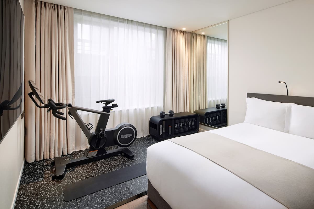 Une chambre d’hôtel avec un lit, un tapis de course et un miroir.