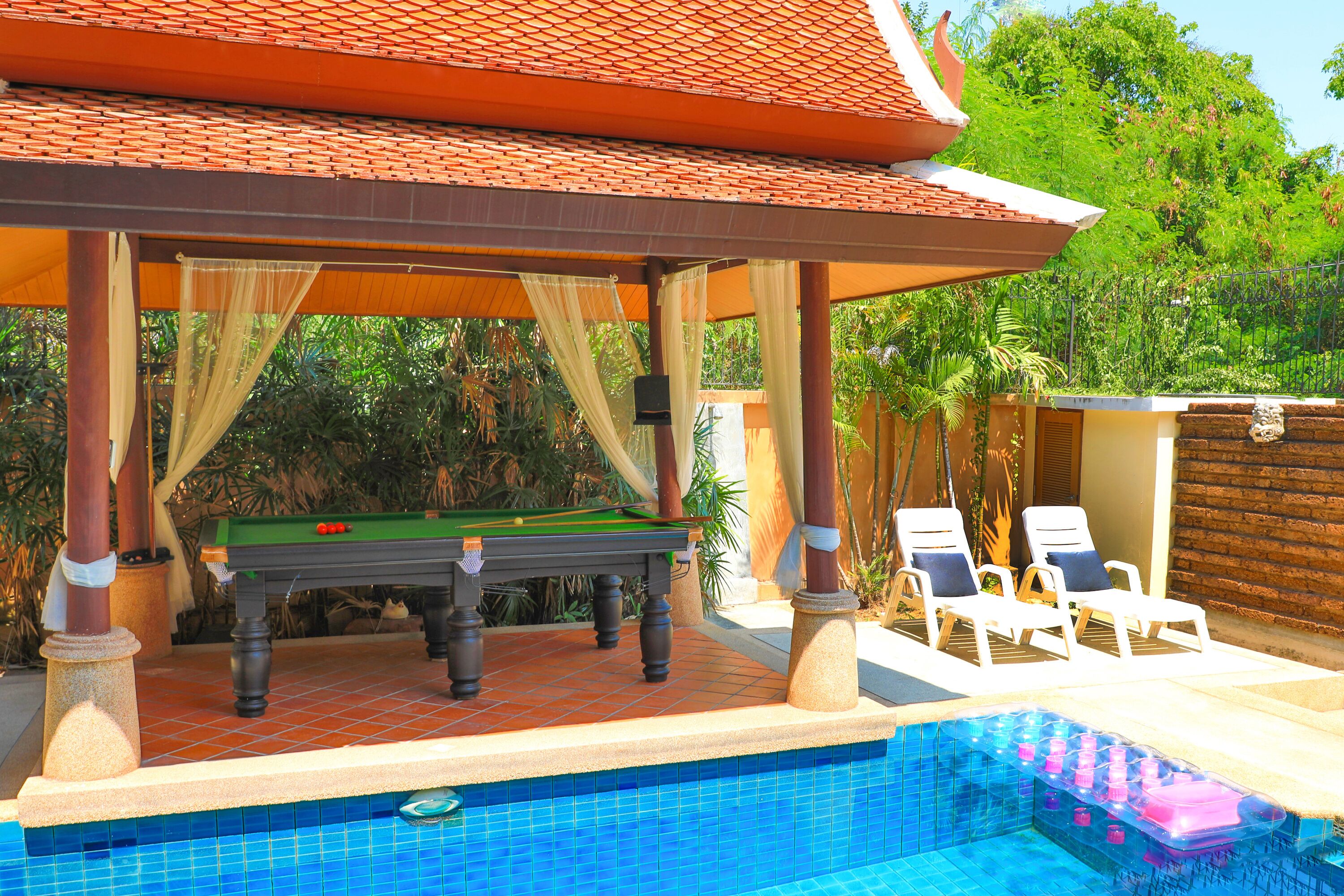 A pool area with a green pool table, lounge chairs, and a covered seating area.