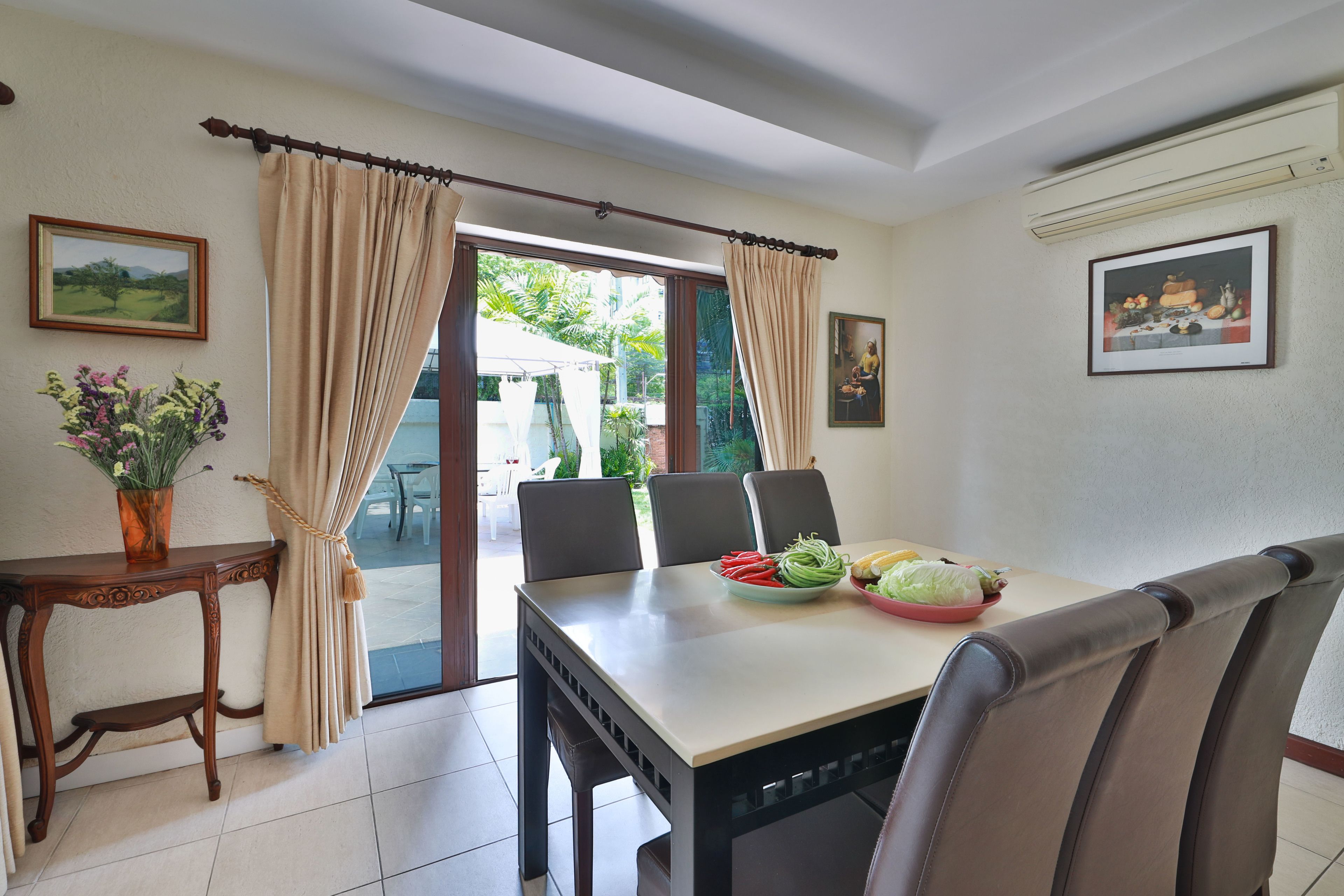 Un coin repas avec une table dressée pour quatre personnes, un vase de fleurs et une vue sur l’extérieur.