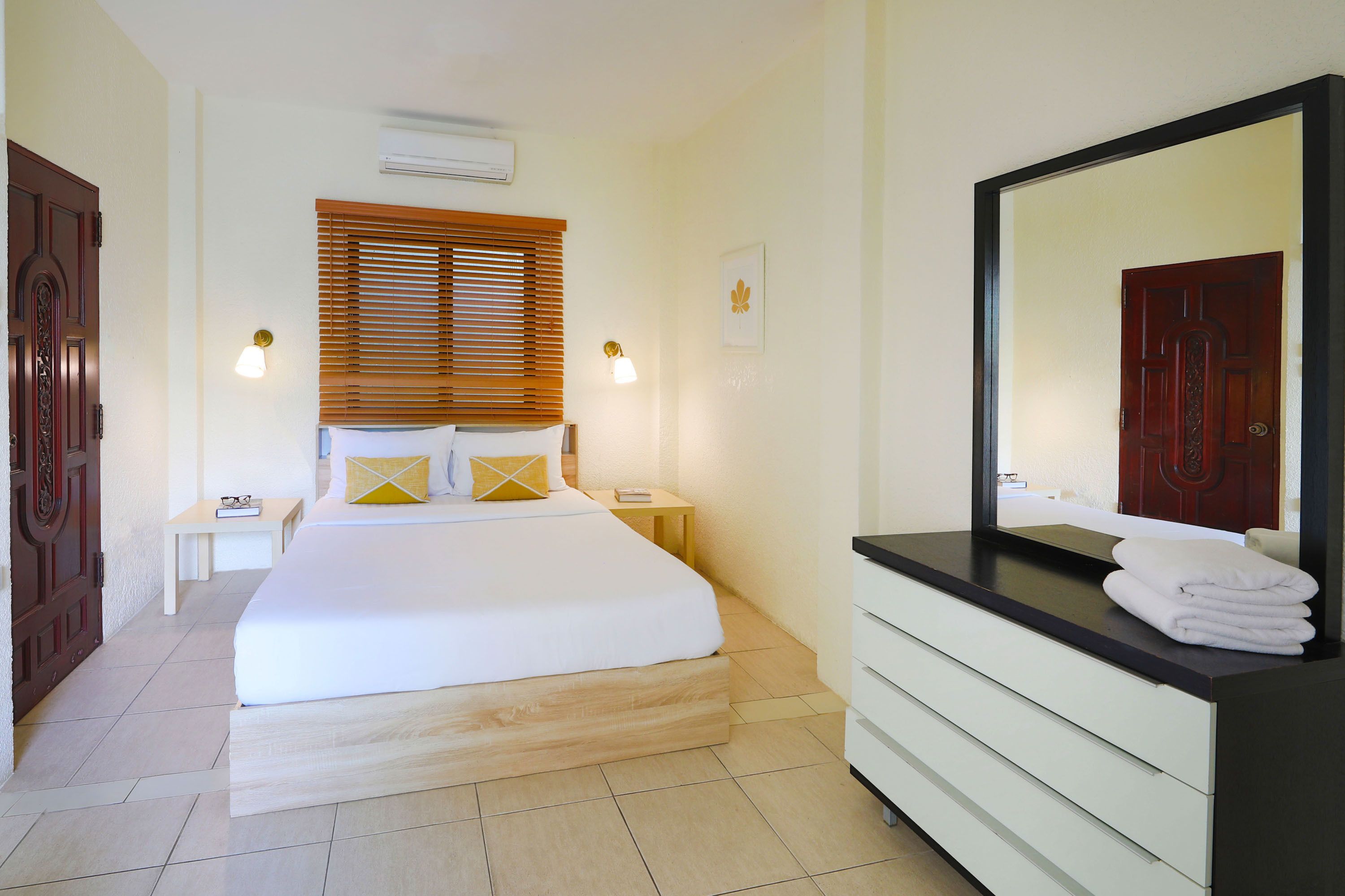 A hotel room with a bed, bedside tables, a vanity with a mirror, and a window with blinds.