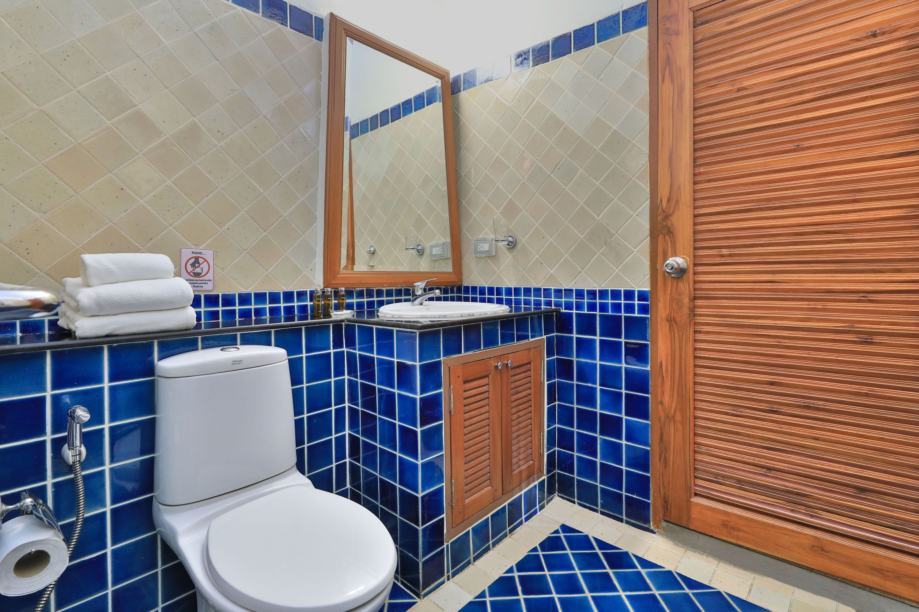 A bathroom with a toilet, sink, mirror, and wooden door.