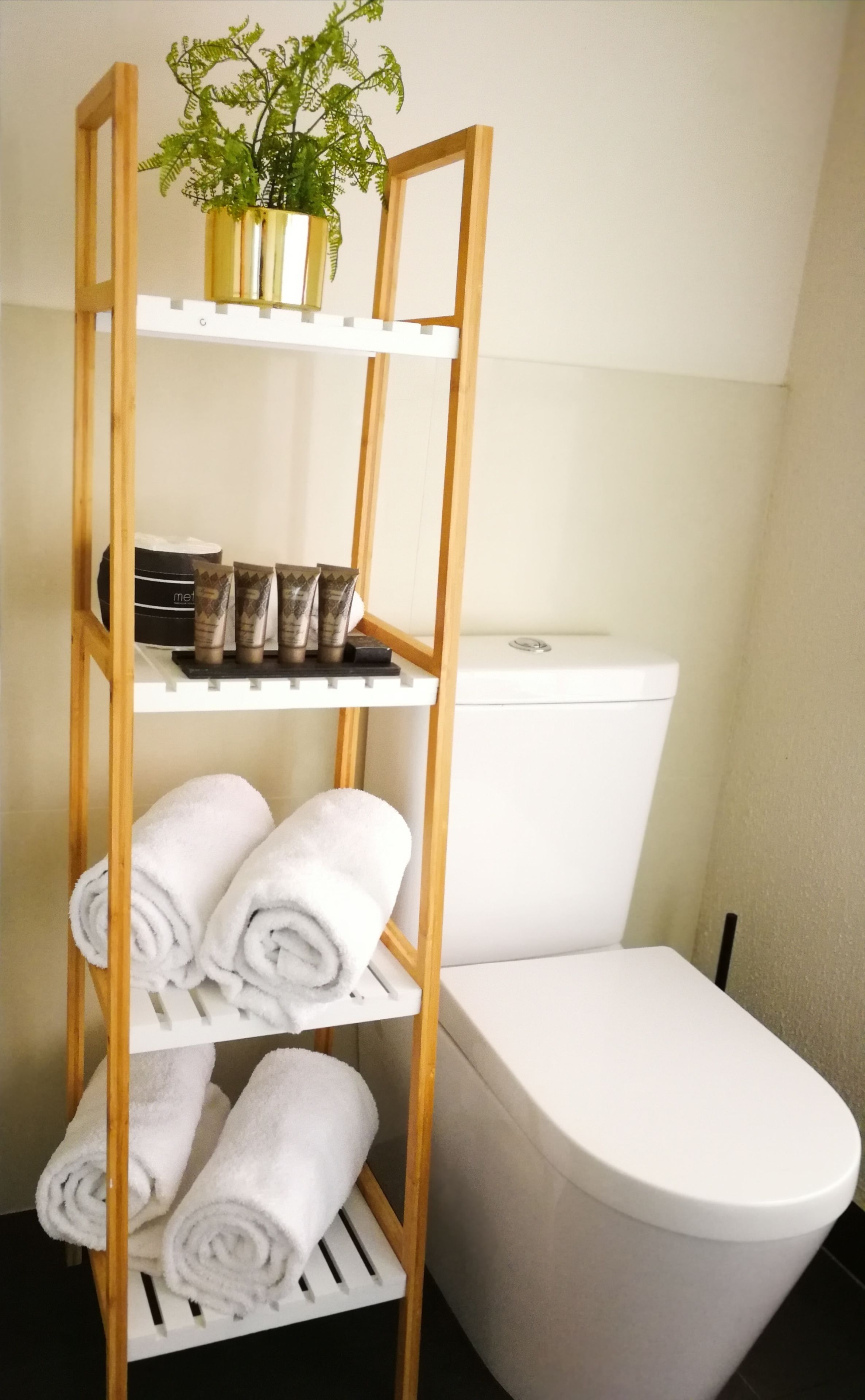 A bathroom with a wooden shelf holding toiletries, towels, and a potted plant.