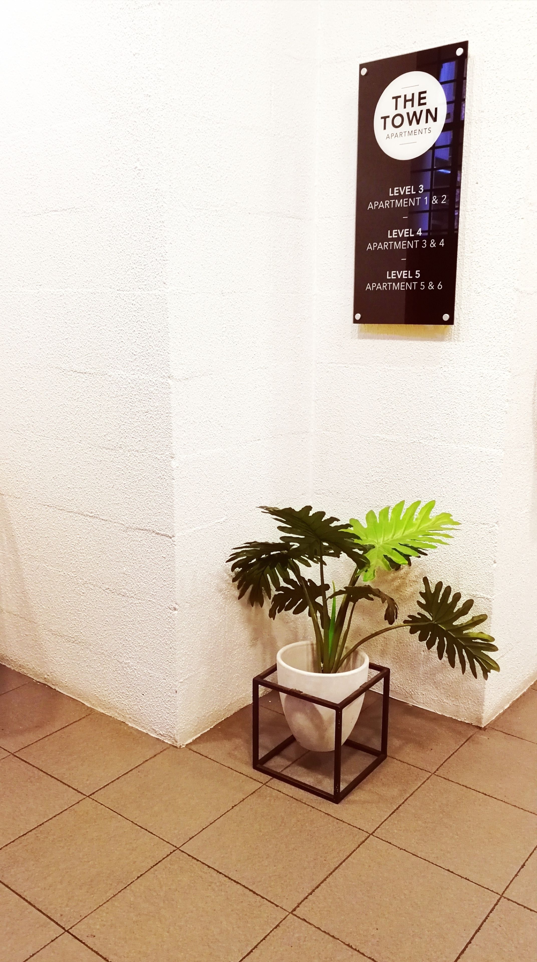 Señal que indica los niveles de los apartamentos y una planta en maceta sobre un suelo de baldosas.