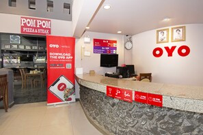 Un espace d’accueil d’hôtel avec un comptoir, un restaurant POM POM Pizza & Steak et un téléviseur fixé au mur.