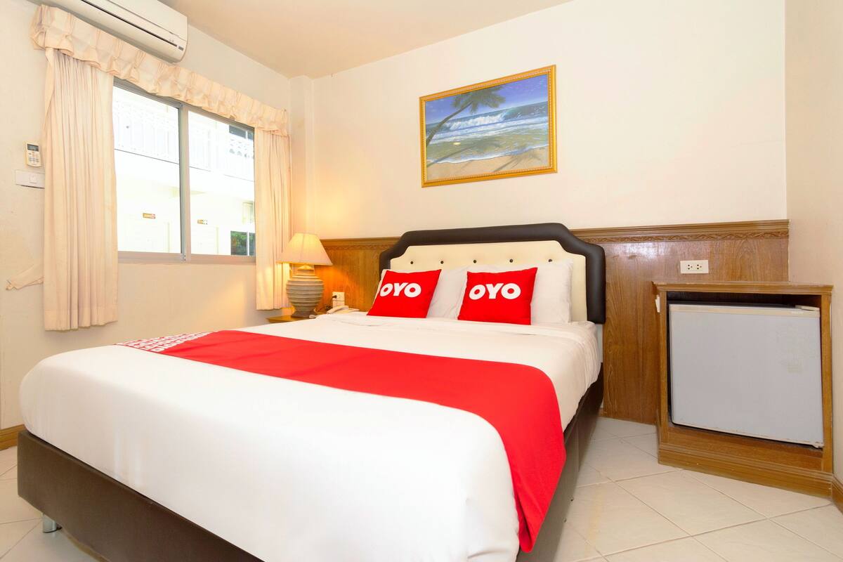 Een hotelkamer met een bed, een schilderij van een strandlandschap en een kleine koelkast.