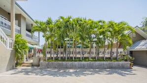 A courtyard with palm trees, a concrete planter, and a building with balconies and a covered area. - Pom Pom Residence (Hua Hin)