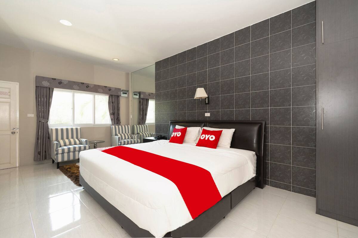 Een moderne hotelkamer met een groot bed, donkere betegelde muren, een raam met gordijnen, een klein tafeltje en een bank.