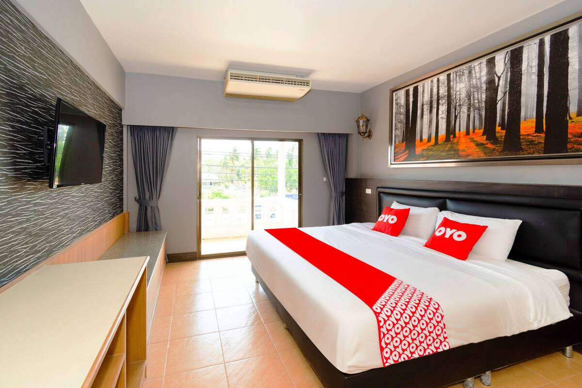Een hotelkamer met een groot bed, een flatscreen televisie aan de muur, een boslandschap op een schilderij en een schuifpui naar een balkon.