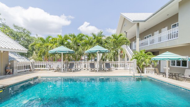 A swimming pool with lounge chairs and umbrellas, surrounded by palm trees and a building with balconies. - Pom Pom Residence (Hua Hin)