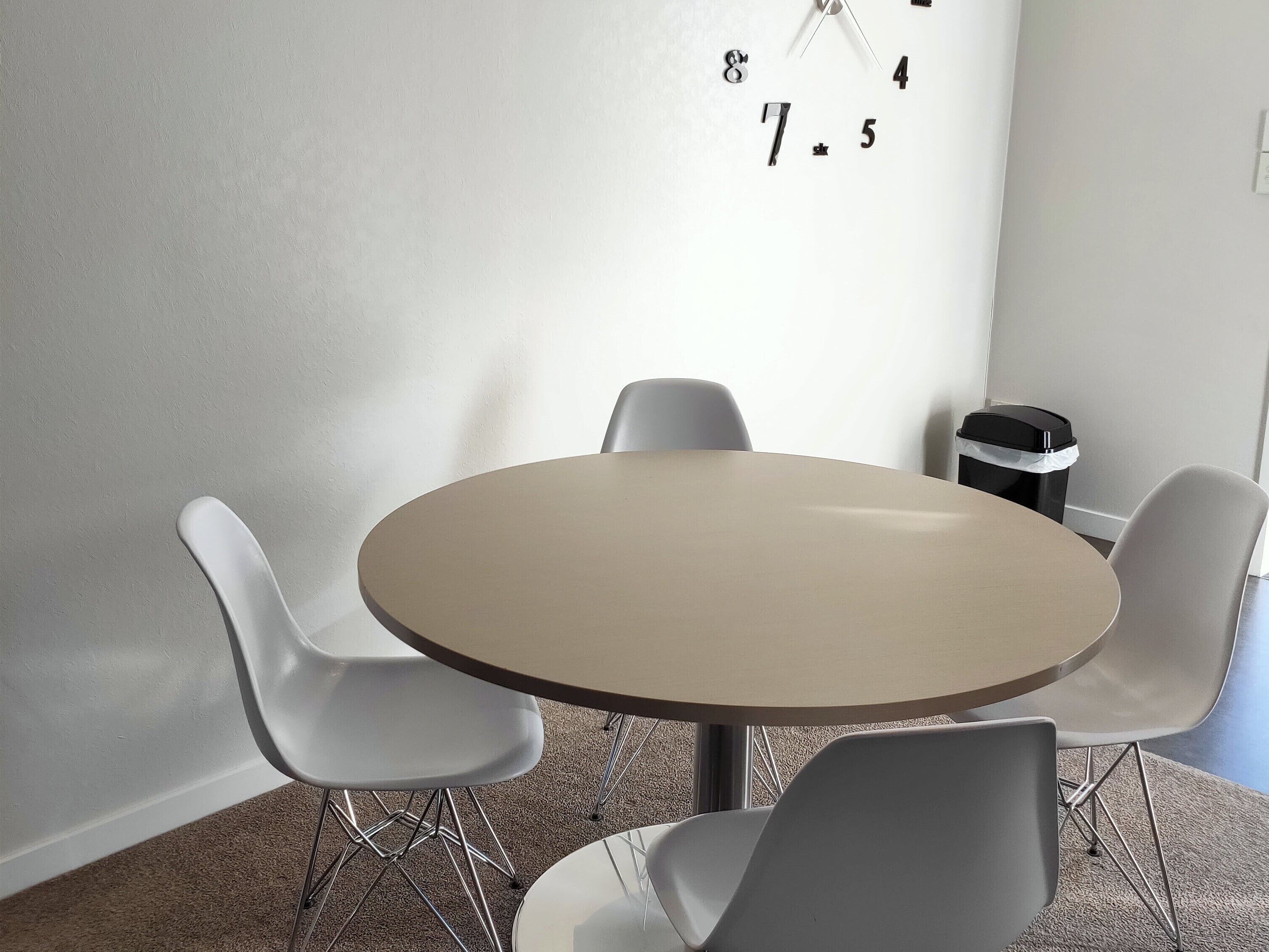 A conference room with a round table, four white chairs, and a clock on the wall.