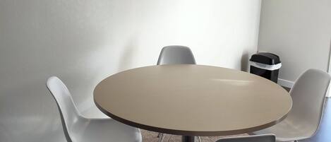 A conference room with a round table, four white chairs, and a clock on the wall.