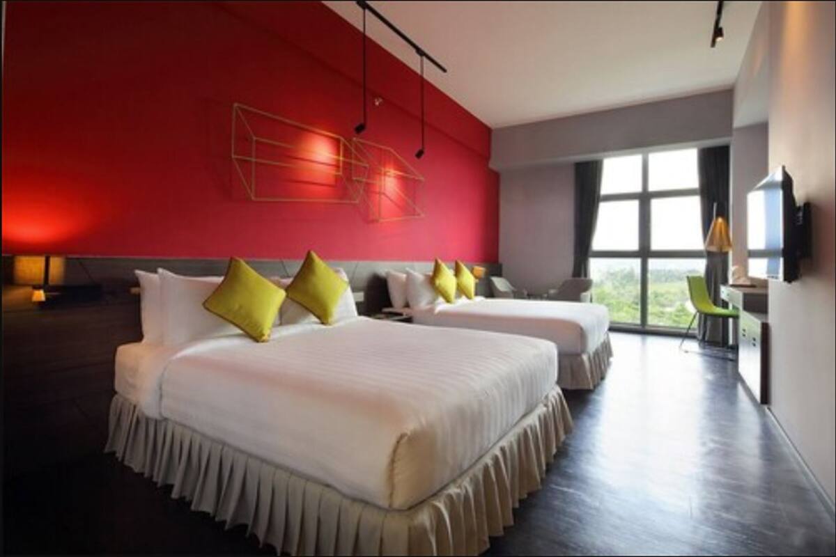 Een moderne hotelkamer met twee bedden, een rode accentmuur en een groot raam met uitzicht.