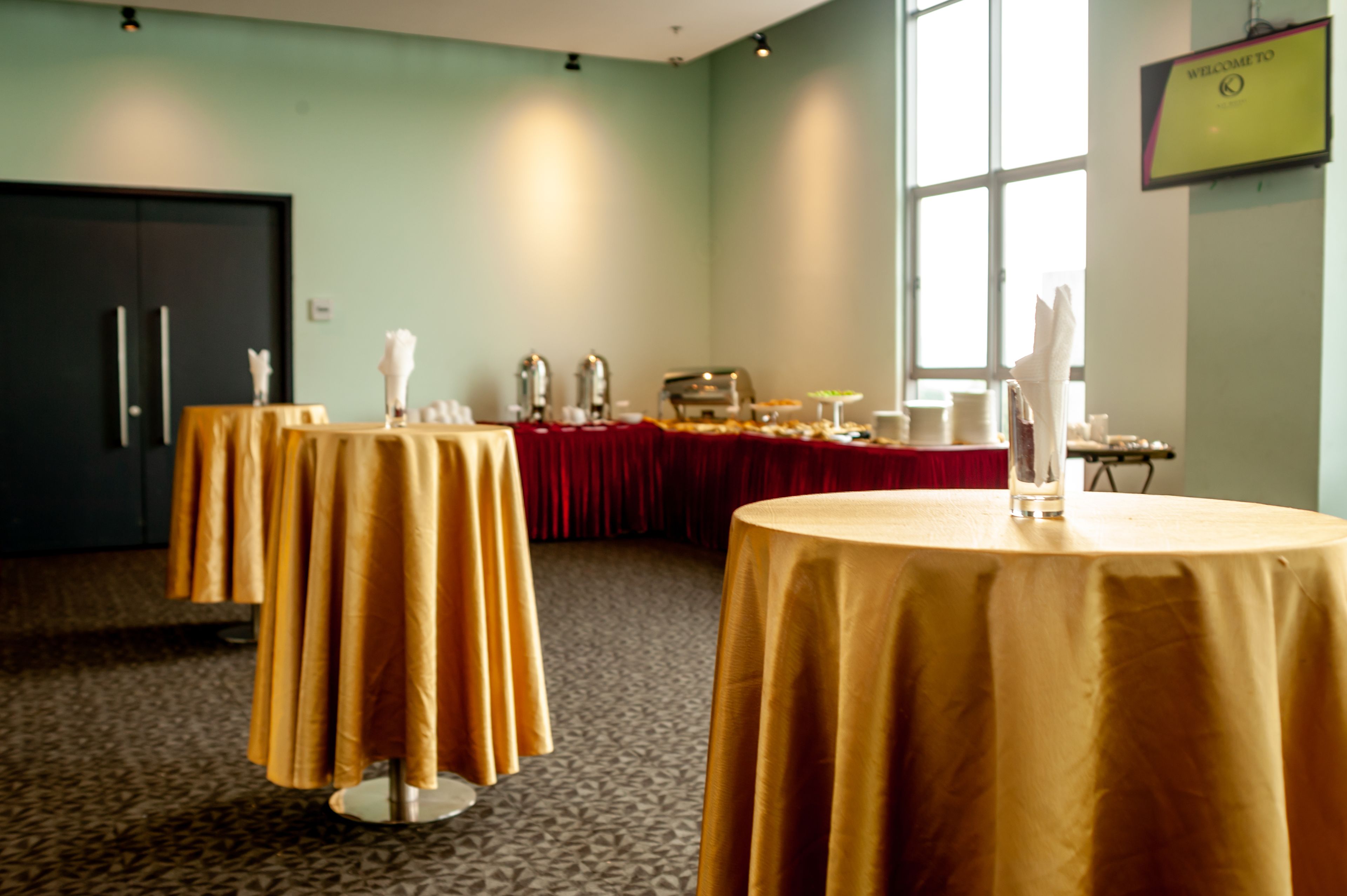 A conference room with round tables covered in gold tablecloths, a red draped table, and a 'Welcome to' sign on the wall.