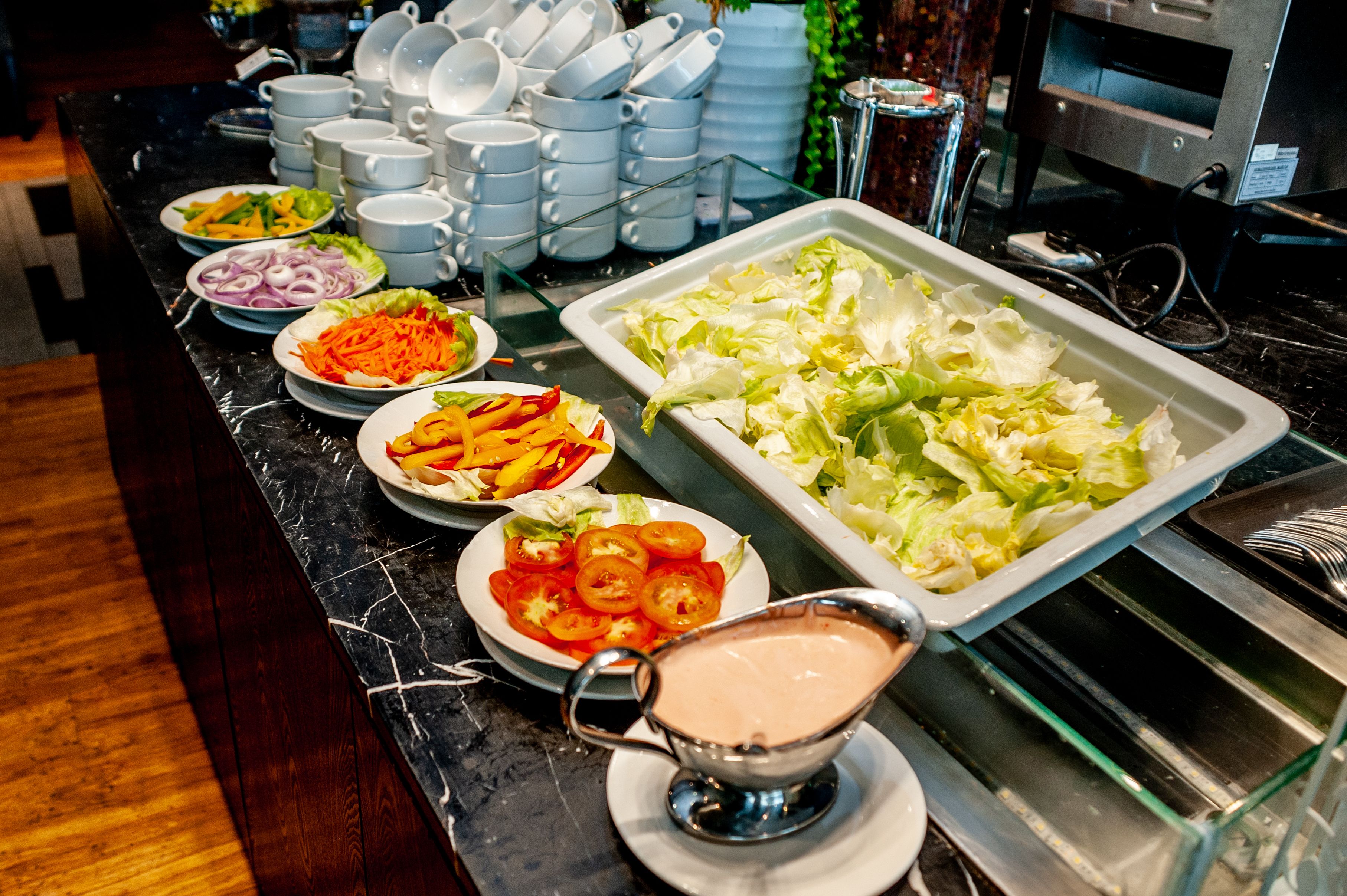 Un bufé con diversos platos, incluyendo ensaladas, verduras y un dispensador de salsa.